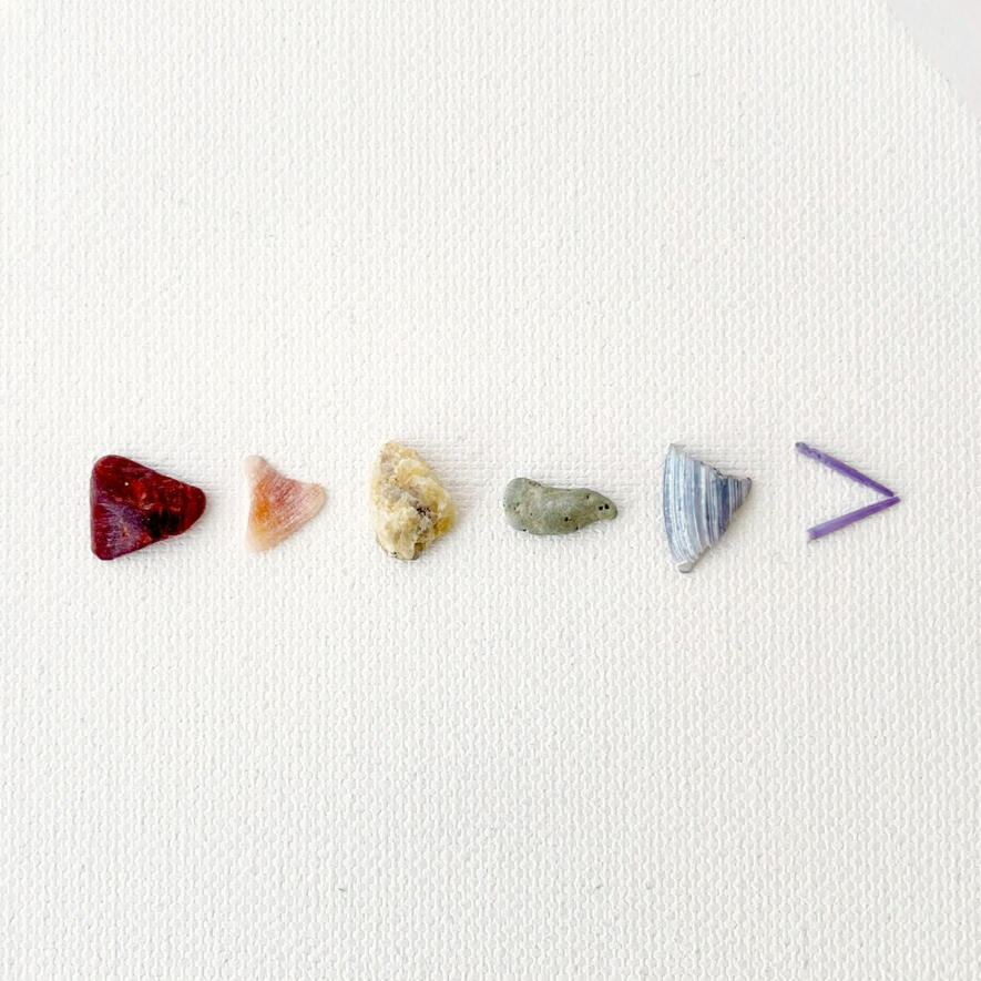A rainbow array of pebbles and shell fragments, lined up horizontally, all evoking triangles.