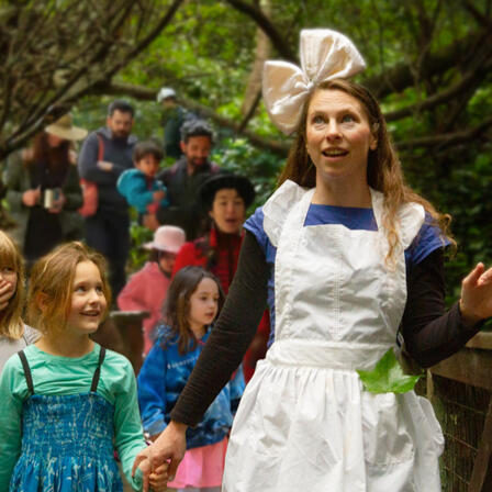 Juliana Frick, dressed as Alice, leads a group of families through the forest.