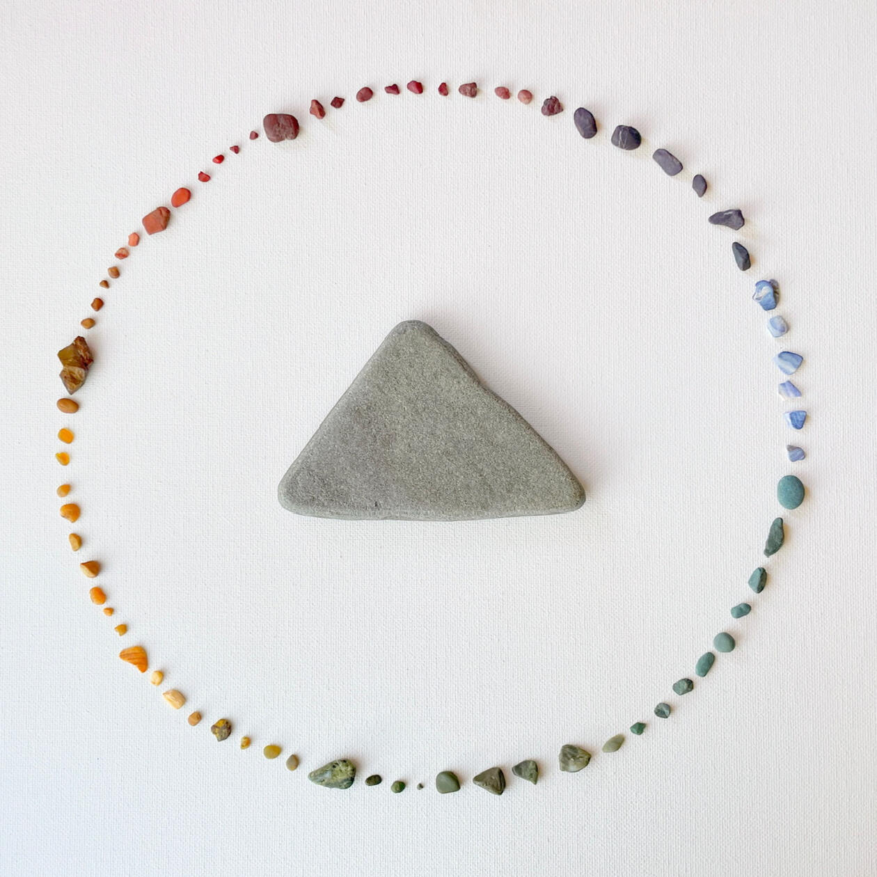 A rainbow array of pebbles arranged in a circle around a central gray triangular stone.